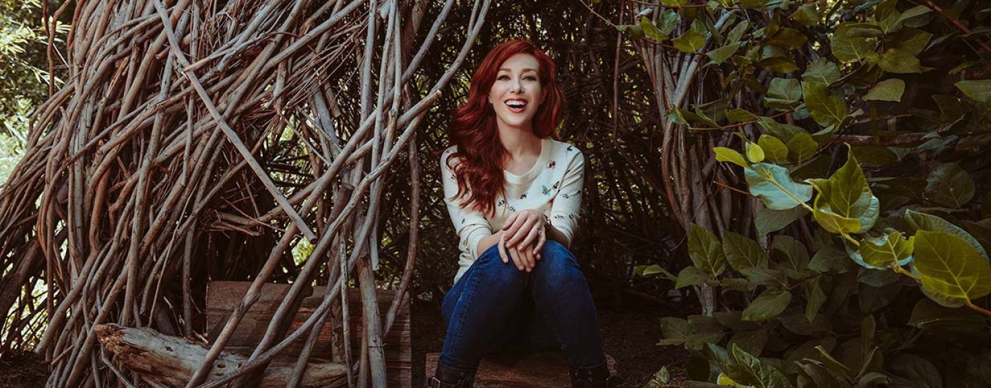 Red haired woman sitting inside entwined tree branches looking like a hut